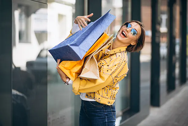 Lachende junge Frau mit bunten Einkaufstüten in der Stadt als Symbol für positive Emotionen beim Einkaufen durch strategisches Emotional Branding von foxdot.me.
